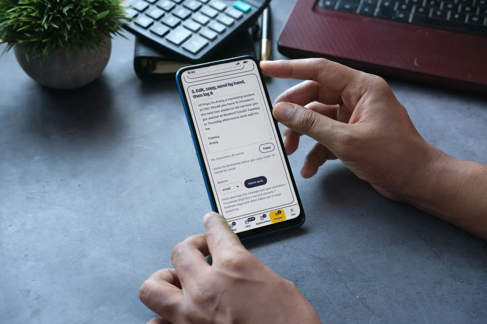A hand reaches for a phone on a desk showing a short note to a contact in the Coffee To Career app, with sample data.