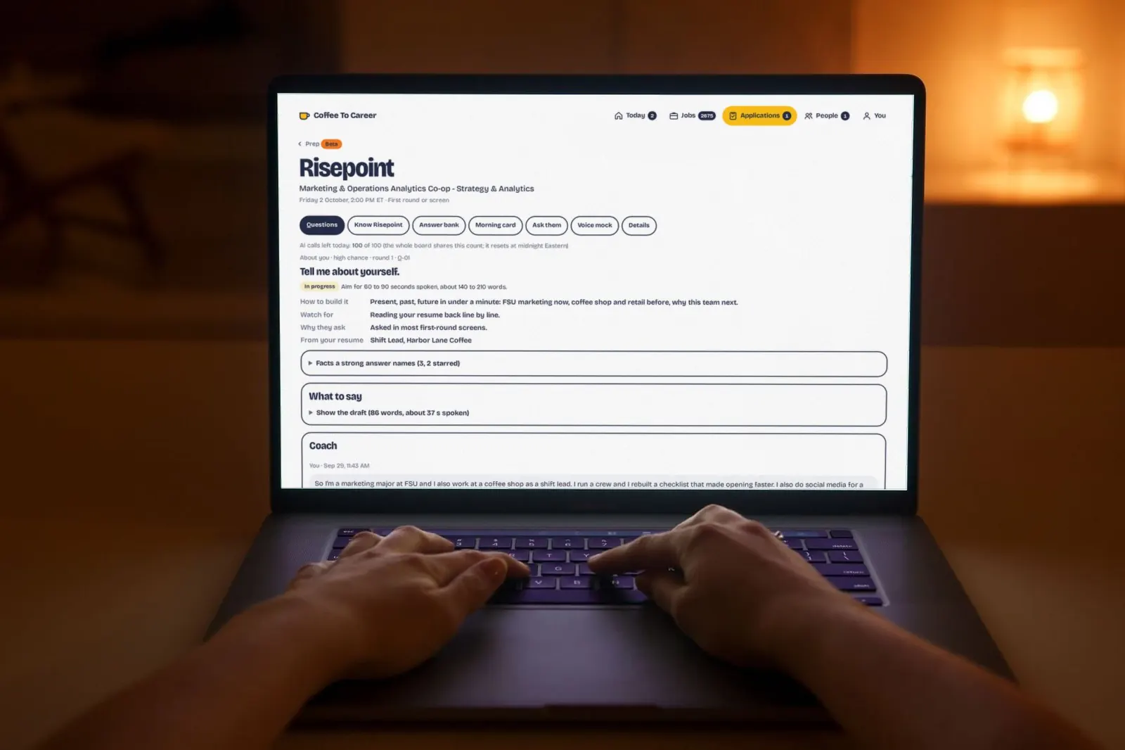 Hands on a laptop keyboard in a warm, lamp-lit room at night, the Coffee To Career interview prep page on screen with sample data.