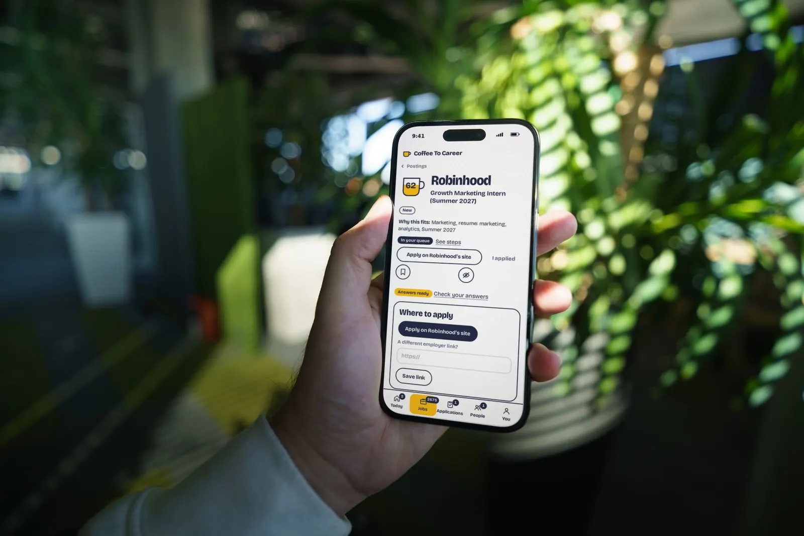 A hand holds up a phone showing a Robinhood internship posting in the Coffee To Career app, with sample data.