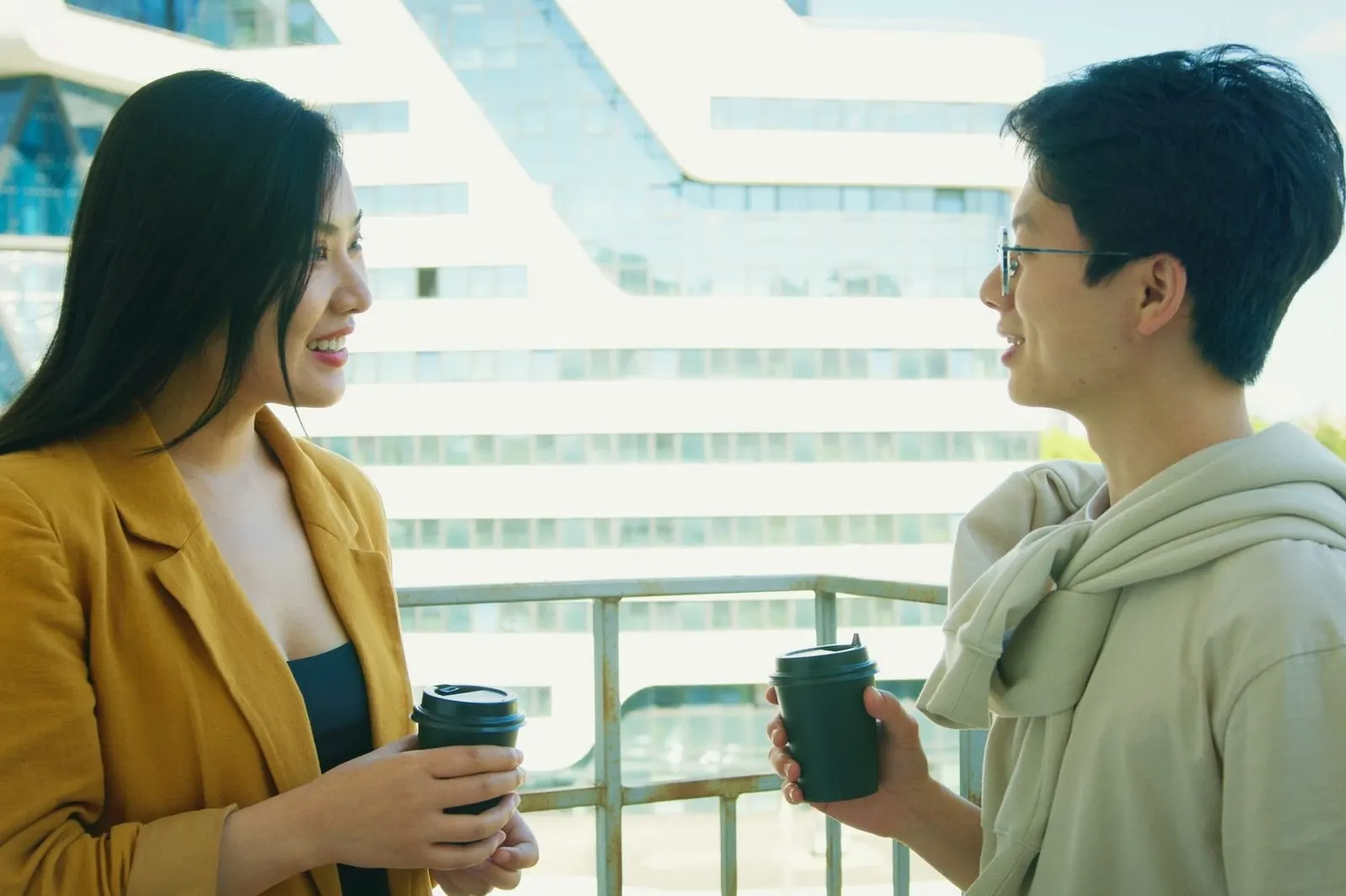 Two young people talk over takeaway coffee on a balcony.